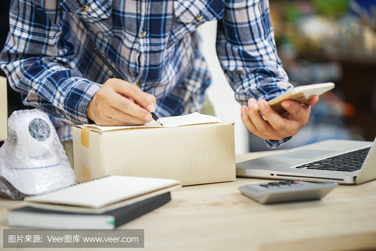 年輕的創(chuàng)業(yè)小企業(yè)主在工作場(chǎng)所的盒子里裝攝像頭閉路電視。自由職業(yè)者銷(xiāo)售者準(zhǔn)備產(chǎn)品的包裝過(guò)程在家里。網(wǎng)絡(luò)銷(xiāo)售,網(wǎng)絡(luò)營(yíng)銷(xiāo),